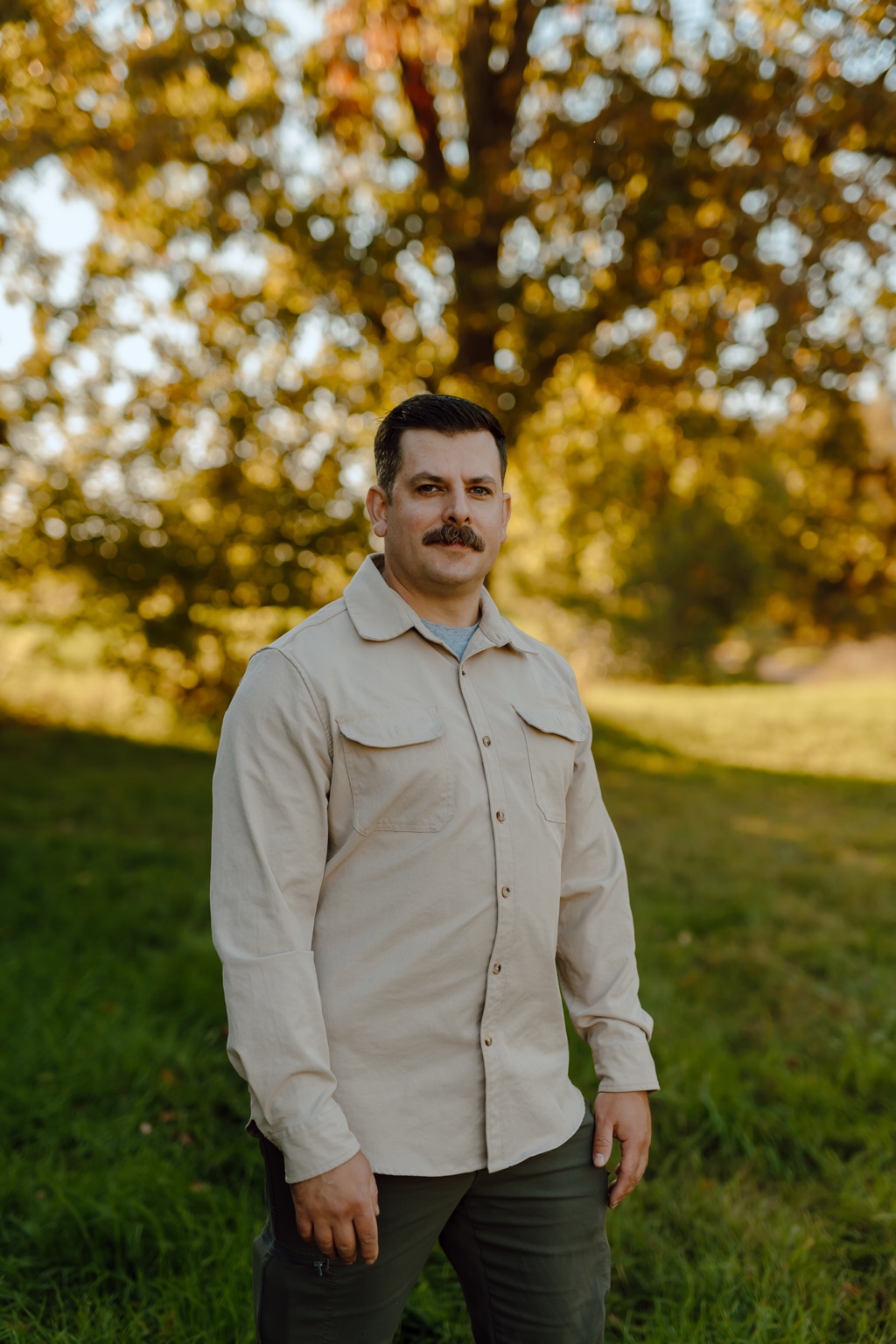 Damian Hansen standing outdoors in a field with autumn trees in the background.