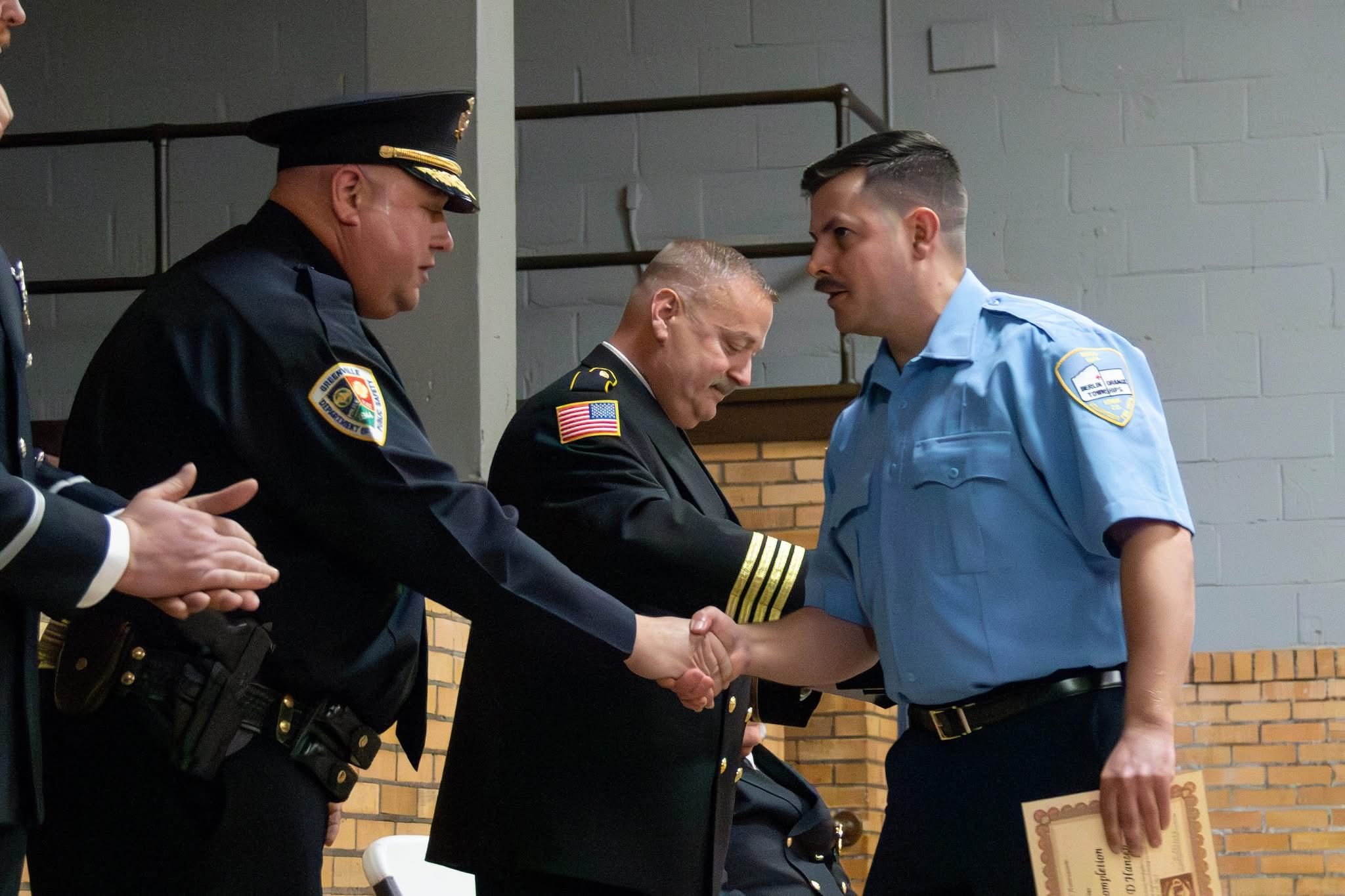 Damian Hansen shaking hands during a fire department ceremony while holding a certificate.