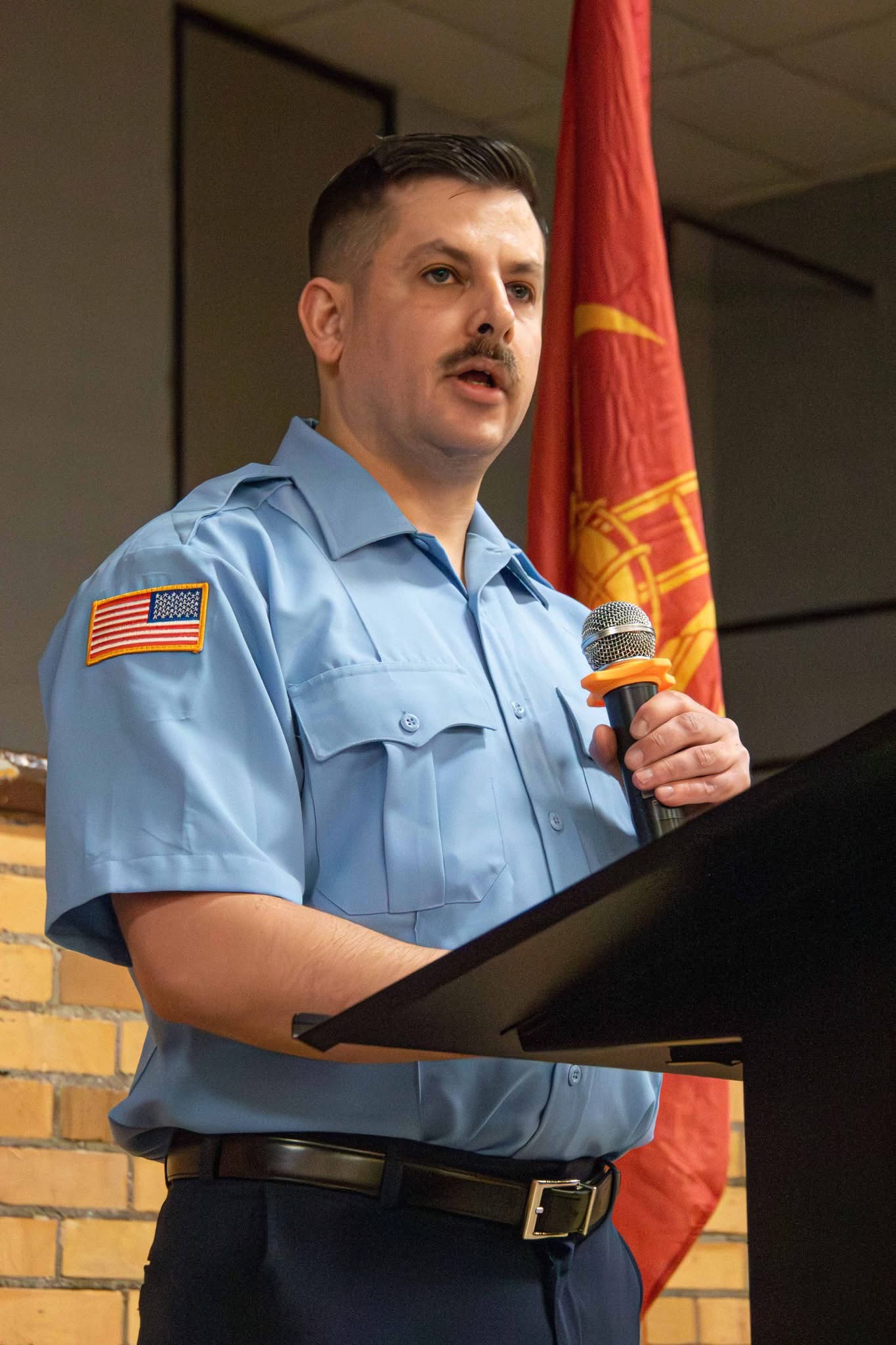 Damian Hansen speaking at a podium in a fire department uniform while holding a microphone.